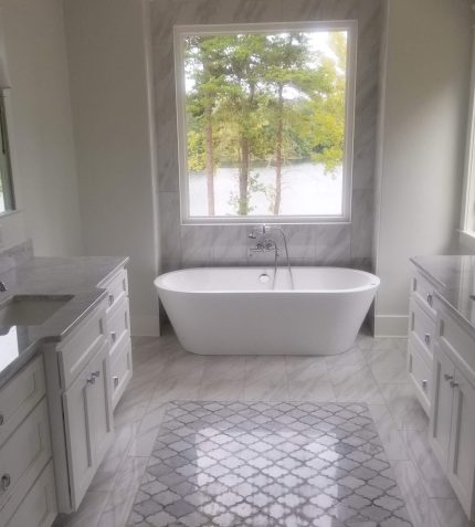 A spacious bathroom featuring a large tub beneath a wide window, allowing natural light to fill the room.