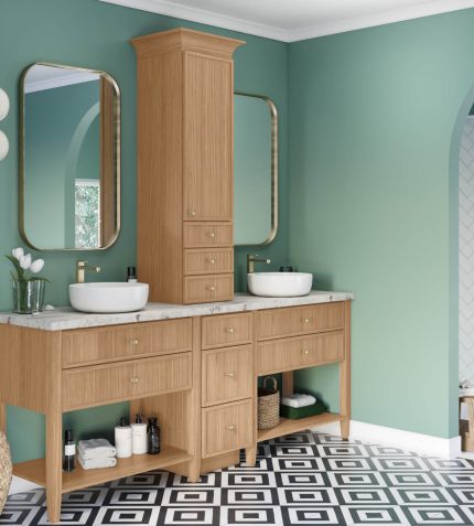 A modern bathroom with a wood vanity, marble countertop, round sinks, green walls, and a patterned floor. Shelves hold toiletries and decor.