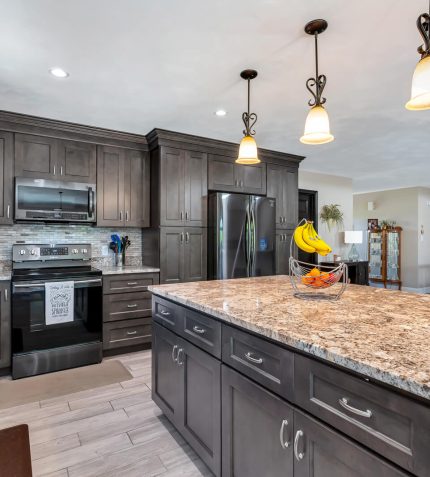 Modern kitchen featuring white cabinetry, stainless steel appliances, a marble countertop island, and wooden floors, with a fruit basket.