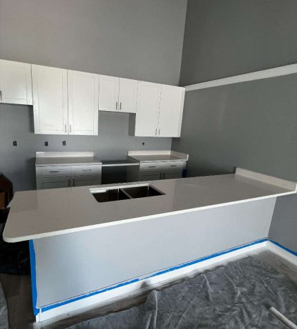 A kitchen featuring white cabinets and countertops is being painted, showcasing a fresh renovation process.