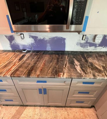 A kitchen counter with blue tape applied across its surface, indicating an area for repair or painting.