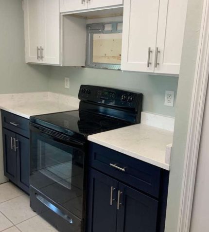 Modern kitchen with black stove, dark blue cabinets, and white countertops. An open shelf above the stove adds to the design.