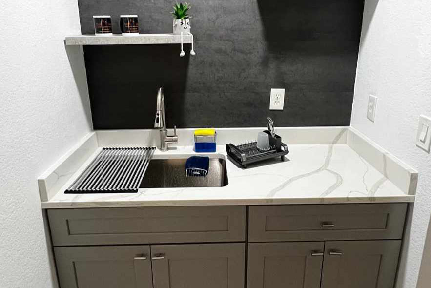 A kitchen sink set against a black wall, featuring a sleek white countertop.