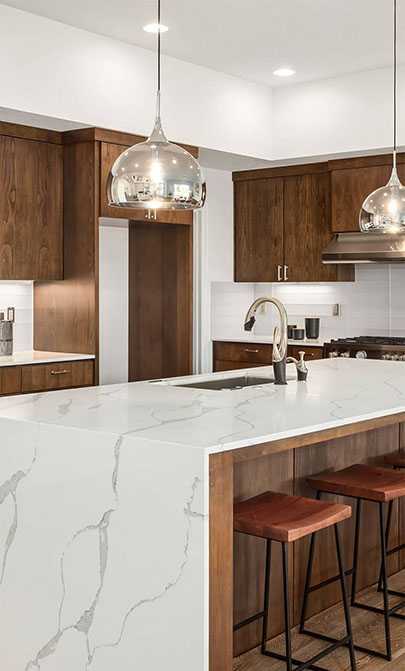 Modern kitchen featuring a white marble countertop, wooden cabinetry, and sleek pendant lights above wooden bar stools.